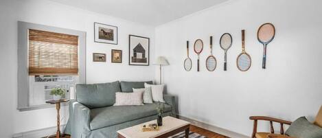 Sala de estar con sofá gris, una mesa de centro, una lámpara y una pared con raquetas de tenis.
