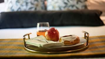 Un plateau avec un verre de jus, une pomme rouge et un beignet, posé sur un lit avec un oreiller à motifs en arrière-plan.