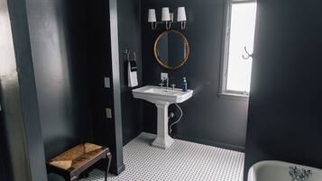 Un baño con lavamanos pedestal, un espejo redondo y un banco.