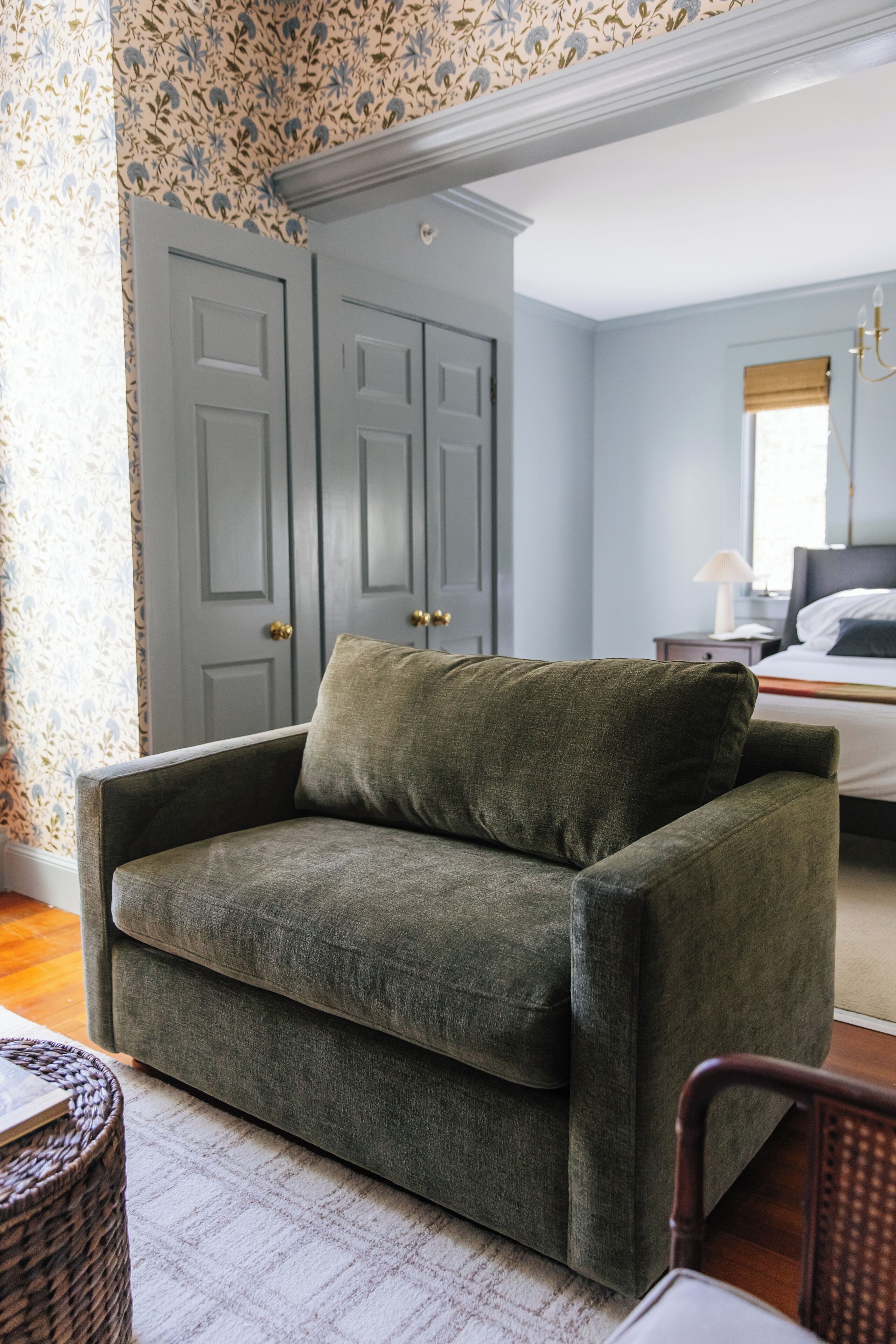 Una habitación con un sofá verde, un sillón de mimbre y una cama con cabecero blanco.