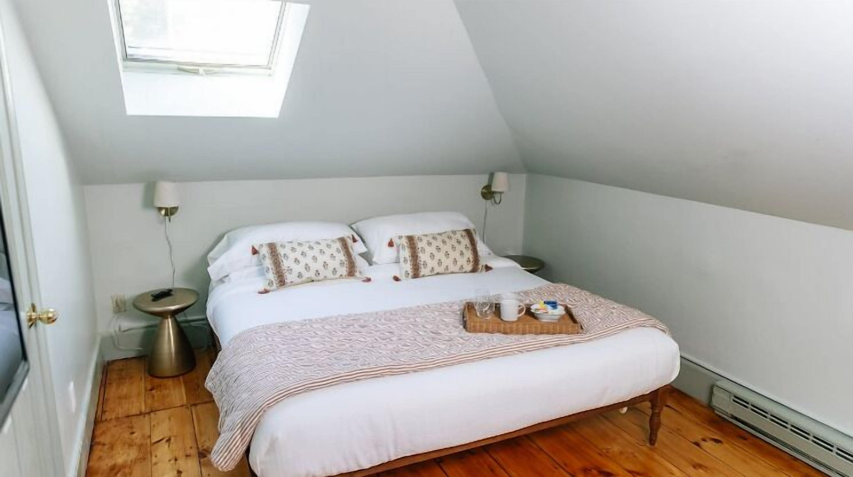 Una cama bien hecha con edredón blanco, dos almohadas y una mesita de noche con lámpara.