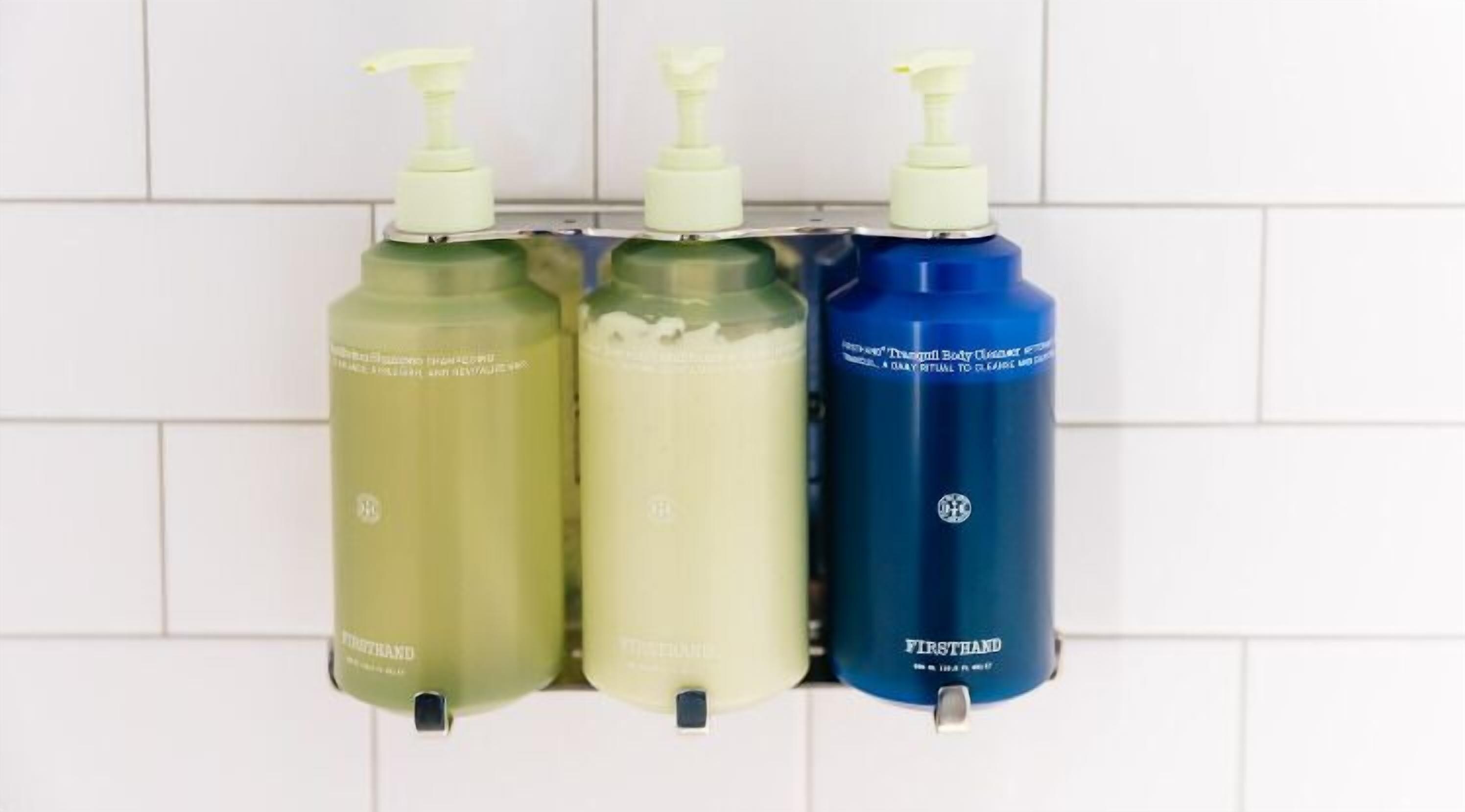 Three bottles of hand sanitizer on a white tiled wall.