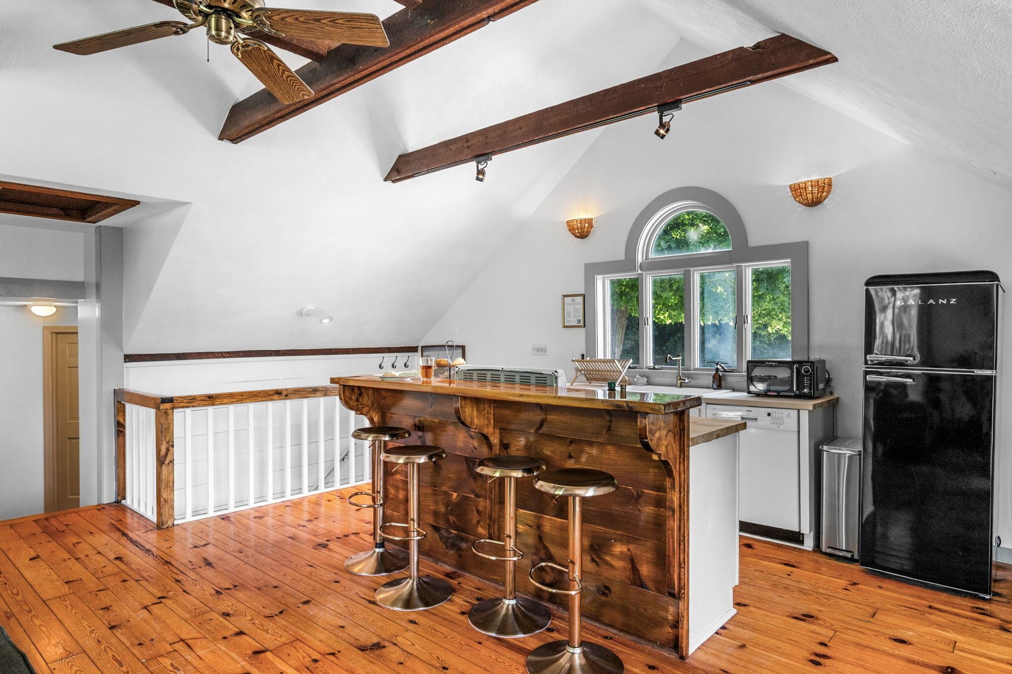 A kitchen with a wooden island, bar stools, a ceiling fan, and a refrigerator.