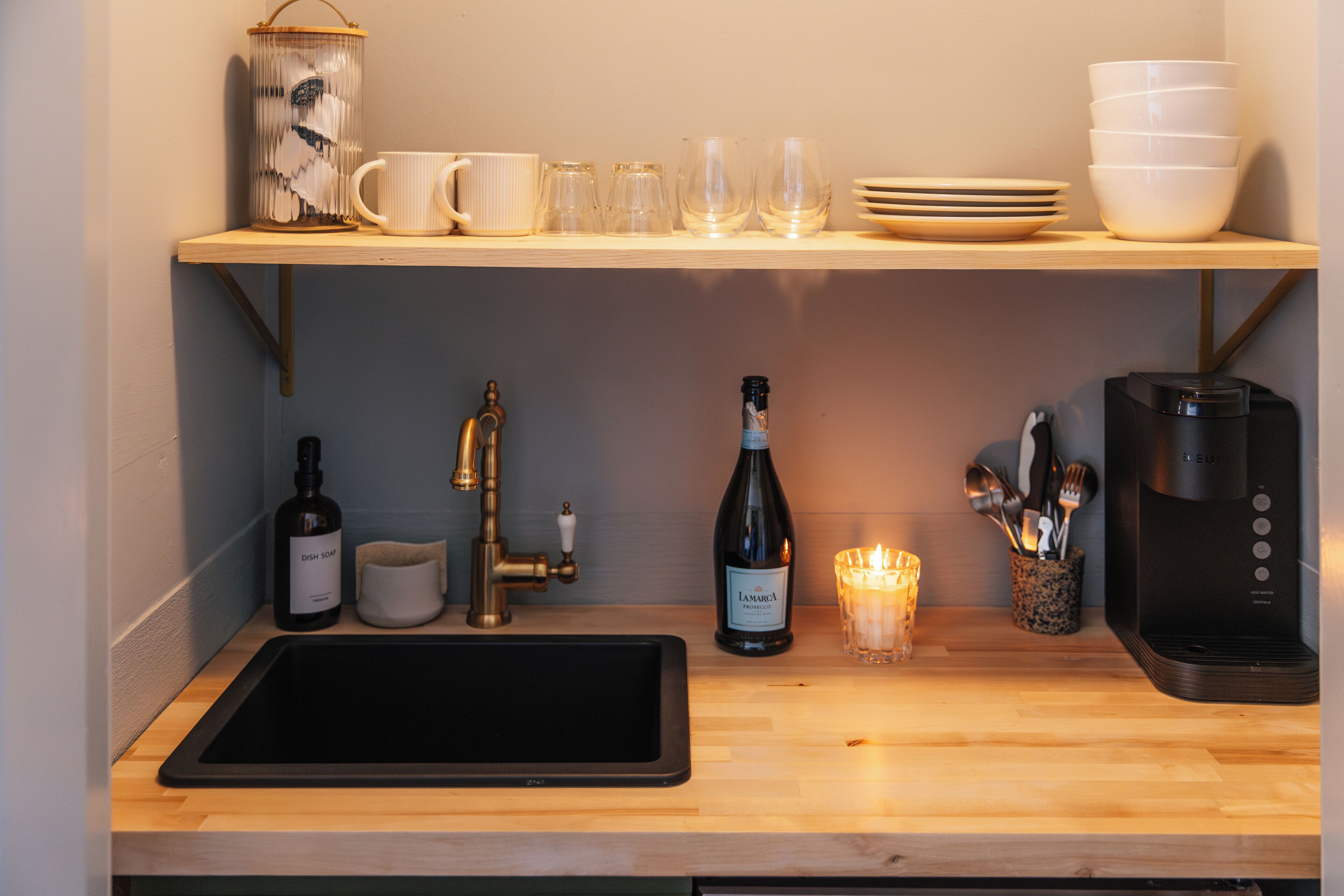 A kitchen counter with a sink, a coffee maker, a bottle of wine, and various glassware.