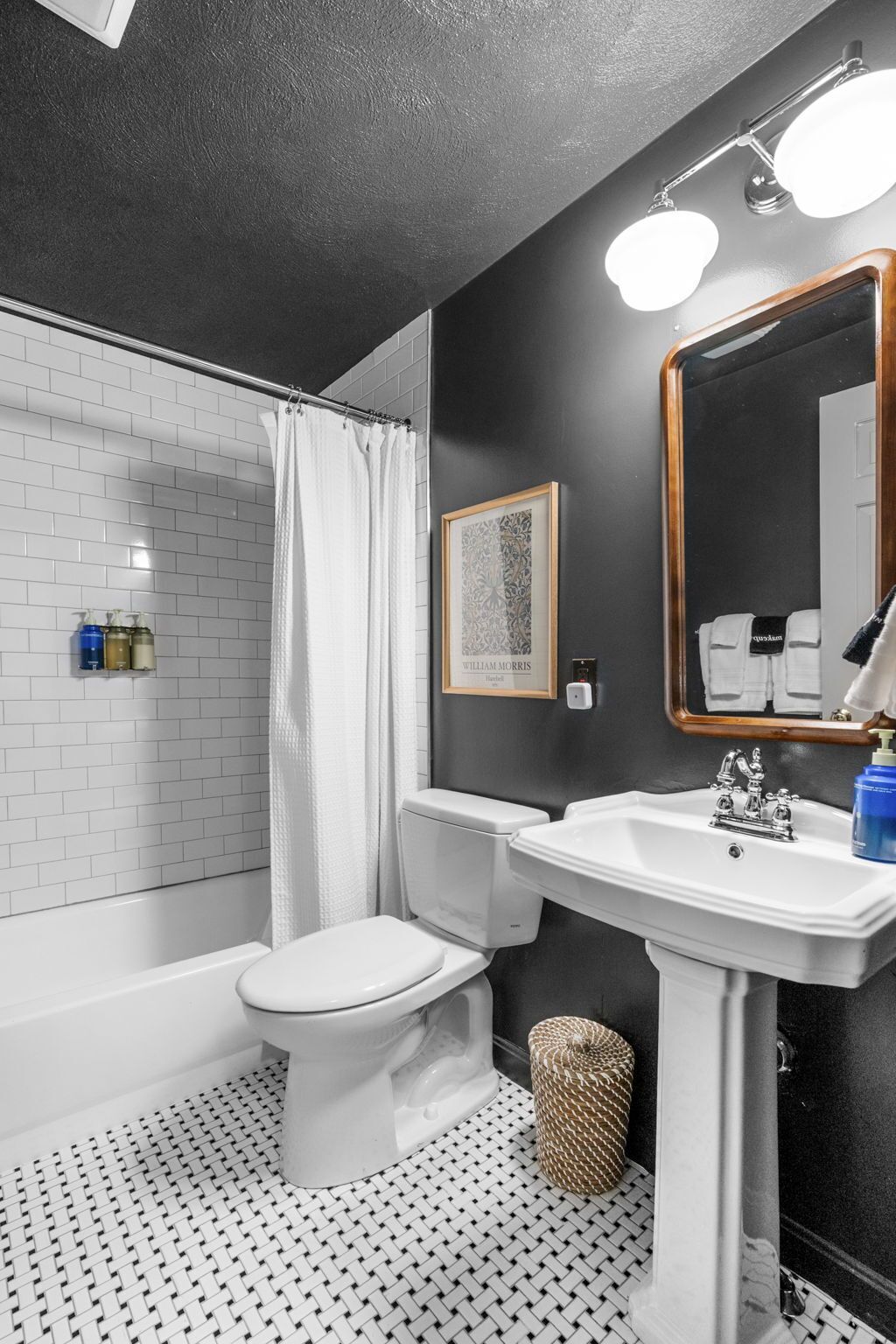 A bathroom with a white toilet, a white sink, and a shower with a white curtain. There is a framed picture on the wall and a mirror above the sink.