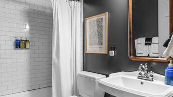 A bathroom with a white toilet, a white sink, and a shower with a white curtain. There is a framed picture on the wall and a mirror above the sink.