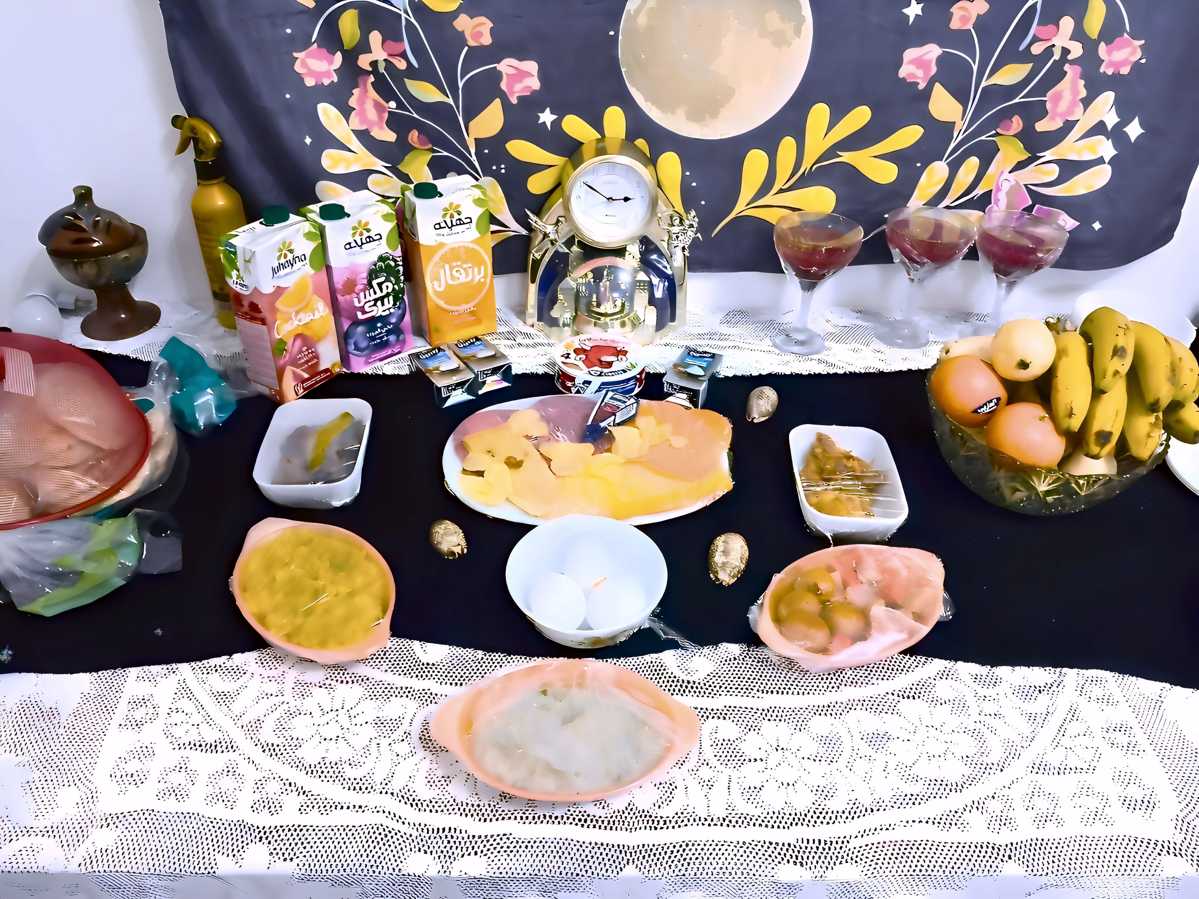 A table with various food items and drinks, a decorative wall, and a clock.