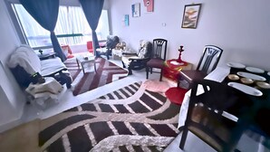 A living room with a sofa, a coffee table, a rug, and a dining table with plates. - Private Rooms in Shared Apartment, Prime Location, Port Said Downtown (Al Zehour)