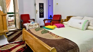 A hotel room with a bed, two red chairs, a small table with a tissue box and glass, and a door with decorative panels. - Private Rooms in Shared Apartment, Prime Location, Port Said Downtown (Al Zehour)