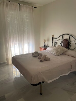 A neatly made bed with rolled towels, a bedside table with a lamp, and sheer curtains. - Los Nidos Apartment, Carihuela (Torremolinos)