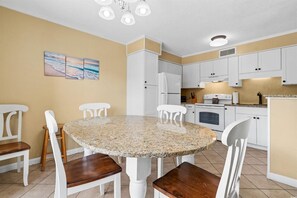 A dining area with a round granite table, white chairs, a white refrigerator, and a microwave.