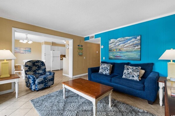 A living room with a blue sofa, a wooden coffee table, and a patterned armchair.