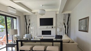 Een moderne woonkamer met een grote televisie, een open haard en een eethoek met krukken.
