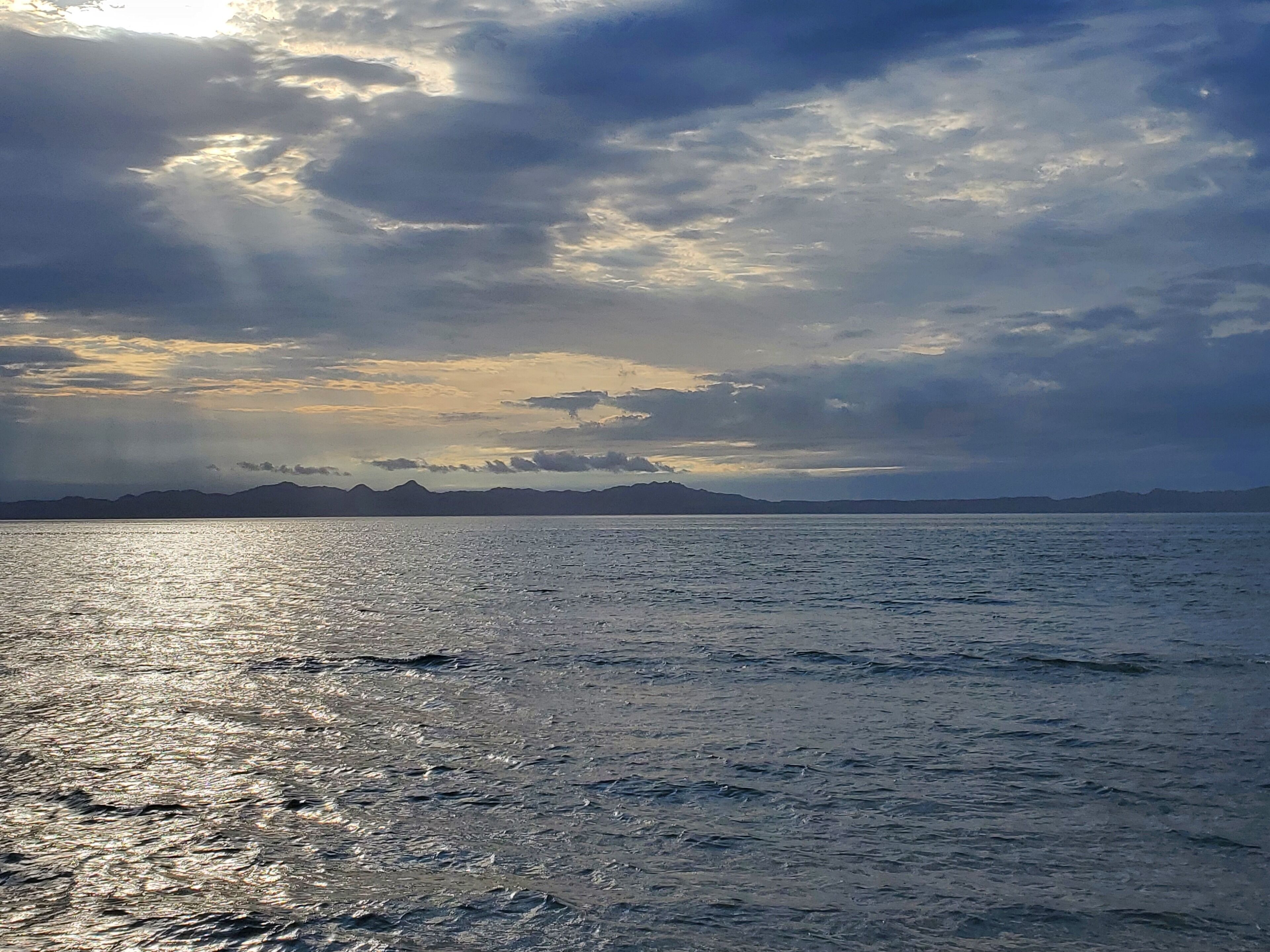 Une mer calme, avec des montagnes lointaines sous un ciel nuageux.
