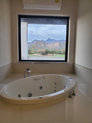 A bathroom with a large bathtub, a window with a mountain view, and a ceiling-mounted air conditioning unit.