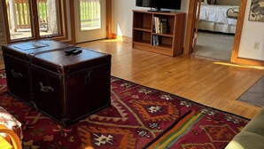 A living room with a wooden floor, a large rug, a vintage suitcase, and a television on a wooden stand.