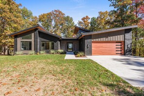 Une maison moderne à deux étages, dotée d’une façade en briques, de grandes fenêtres et d’une porte de garage en bois.