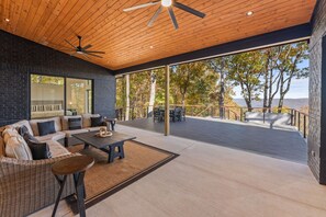 Un espace de vie extérieur moderne, doté d’un plafond en bois, d’un grand ensemble de canapés, d’une table à manger et offrant une vue sur les arbres et les collines.
