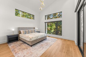 Une chambre à coucher avec un grand lit, deux tables de chevet, une commode et une grande fenêtre donnant sur des arbres.