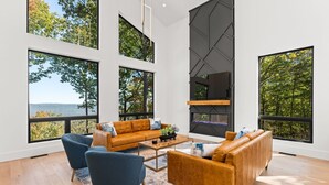 A spacious living room with large windows, a modern fireplace, and a comfortable seating area. - Secluded, modern, spectacular views, hot tub on 18 acres. Firepit,games & more! (Sewanee)