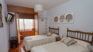 Un dormitorio con dos camas, cabecero de madera, lámpara blanca y una pared decorada con tres motivos de árboles.
