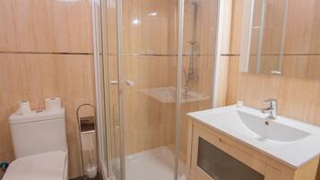 Une salle de bain avec une douche à parois de verre, un lavabo blanc et des toilettes.