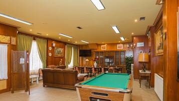 Una mesa de billar en una sala con paneles de madera, un sofá y una televisión.