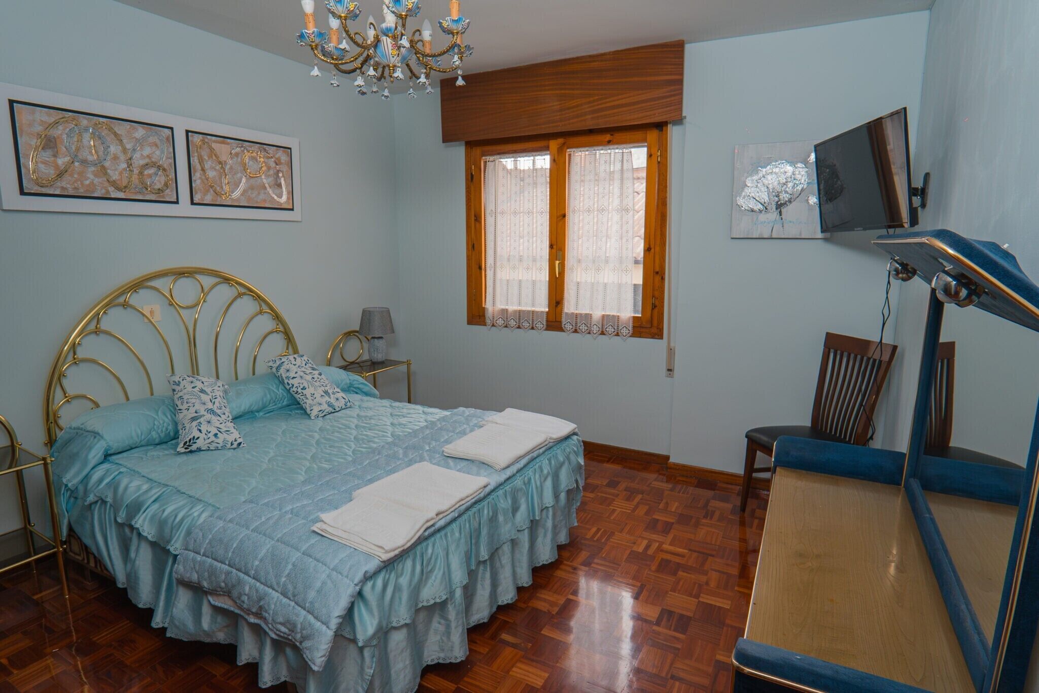 A bedroom with a bed, a desk, a chair, a television, and artwork on the wall.