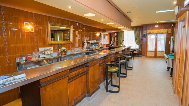 Zona de bar con una barra larga, taburetes y un espejo.