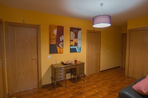 Una habitación con puertas de madera, un escritorio con cajones, dos cuadros en la pared y una lámpara colgante.