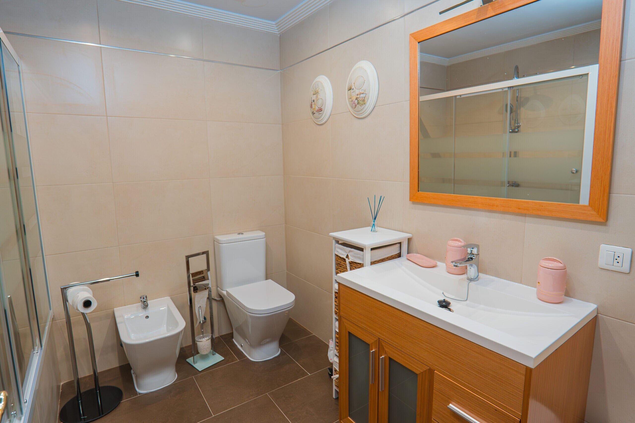 A bathroom with a toilet, bidet, sink, mirror, and a shower area.