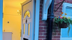 A doorway leading into a room with a white door, a hanging flower basket, and a light fixture on the wall. - Spacious 4BR house close to Gatwick Airport. (Crawley)