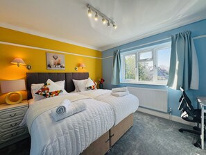 Et soveværelse med seng, sengeborde med lamper, et vindue med gardiner, en radiator og et skrivebord med stol.