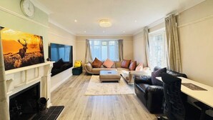 A living room with a fireplace, a sofa set, a television, and a large window. - Spacious 4BR house close to Gatwick Airport. (Crawley)