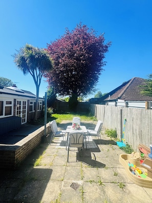 Un jardin avec une table et des chaises de patio, une clôture en bois et un grand arbre aux feuilles roses.