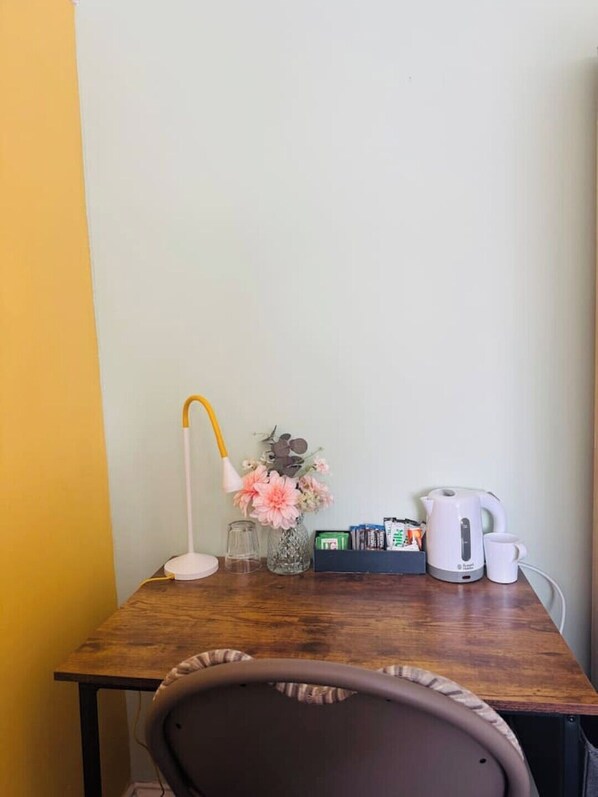 Et træskrivebord med en hvid lampe, en vase med blomster, en elkedel og en kop.