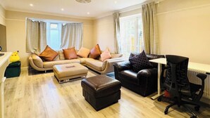 A living room with a sofa, ottoman, and a black office chair. - Spacious 4BR house close to Gatwick Airport. (Crawley)