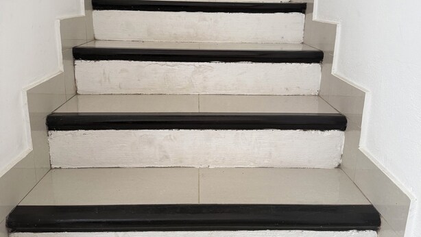 Eine Treppe mit weißen Stufen und schwarzen Kanten, die zu einer Tür oben führt.