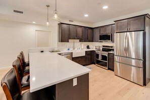 A modern kitchen with dark wooden cabinets, stainless steel appliances, and a white island. - Luxury Condo at Loon (Lincoln)