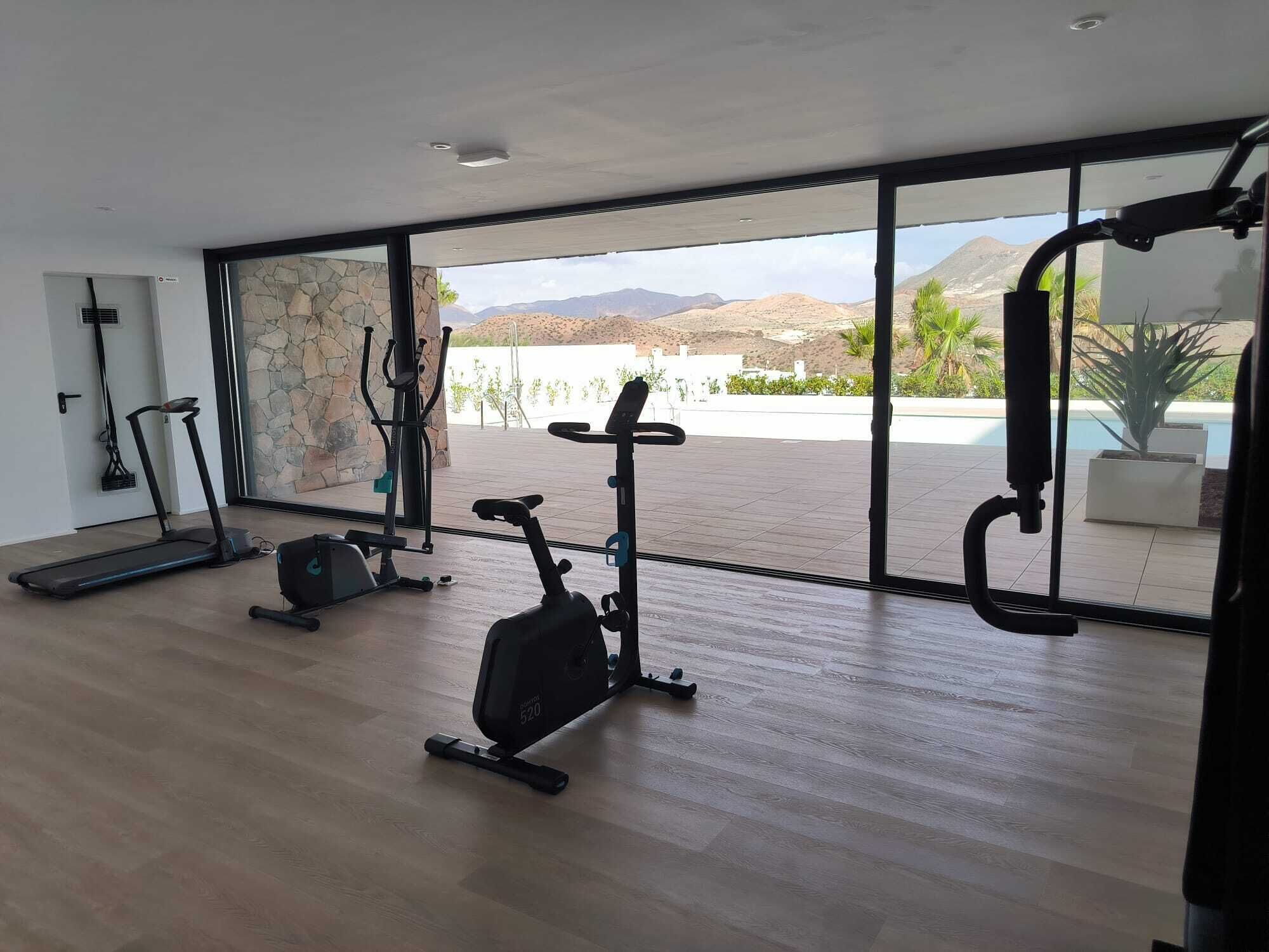 Une salle de sport moderne équipée de matériel d’exercice, dotée de grandes fenêtres et offrant une vue sur les montagnes et une piscine.