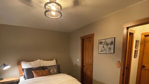 Un dormitorio con cama, mesita de noche, lámpara de pared, puerta y un cuadro en la pared.