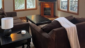 Una sala de estar con chimenea, televisor y ventanas amplias.