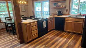 Una cocina con armarios de madera, una estufa y un lavavajillas. En la zona de comedor contigua, hay una mesa y sillas.