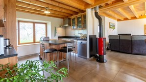 A modern kitchen with wooden beams, a central island with bar stools, a built-in dishwasher, and a red wood-burning stove. - LA MILONGA - AYN - Gîte (AYN)