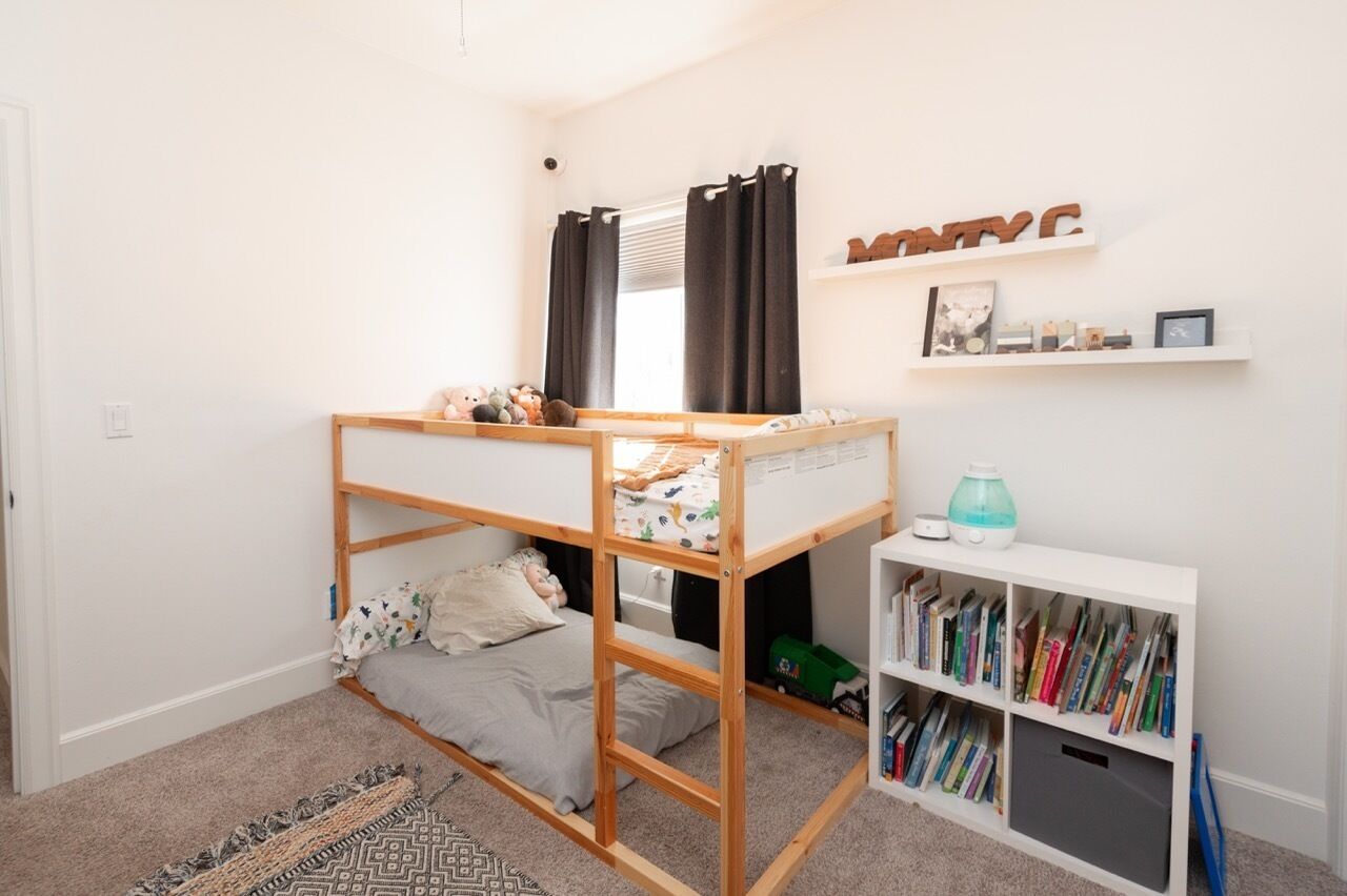 A child's bunk bed with a desk and bookshelf, a window with curtains, and a shelf with decorative items.