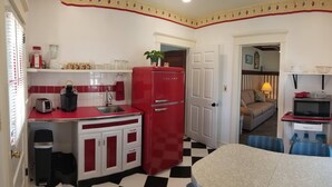 A compact kitchen with a red refrigerator, a toaster, and a sink. A dining area with a table and chairs is visible in the background.