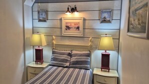 A bedroom with a bed, two bedside lamps, a headboard, and a framed picture on the wall.