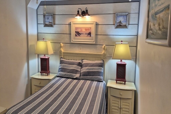 A bedroom with a bed, two bedside lamps, a headboard, and a framed picture on the wall.