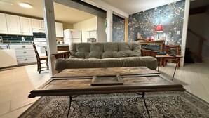 Una sala de estar con un sofá, una mesa de centro, un tapete estampado y una cocina al fondo.