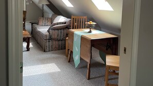 Un dormitorio acogedor en el ático, con techo inclinado, una mesa de madera, una silla, un sofá y una lámpara.